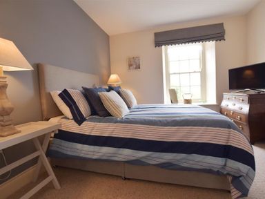 A bedroom with a bed with striped bedding two lamps a window and a chest of drawers with a tv at Gwelfor Newport in Newport Pembrokeshire
