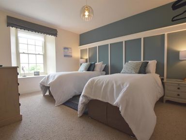 A bedroom with two single beds white bedding and pillows window and dresser at Gwelfor Newport in Newport Pembrokeshire