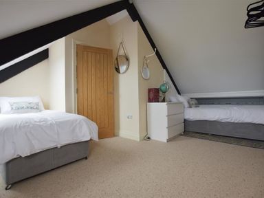 A bedroom with two single beds a wooden door a white dresser with a globe and two mirrors on the wall at Gwelfor Newport in Newport Pembrokeshire