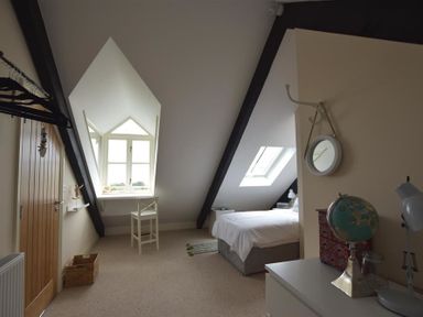 A bedroom with a bed under a skylight a small desk and chair near a window and a globe on a dresser at Gwelfor Newport