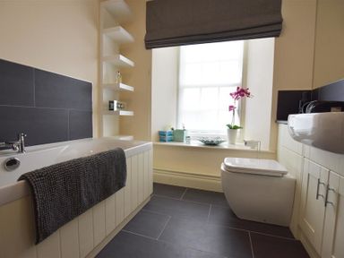 A bathroom with a bathtub and a towel a toilet and a sink near a window with a flower at Gwelfor Newport in Newport Pembrokeshire