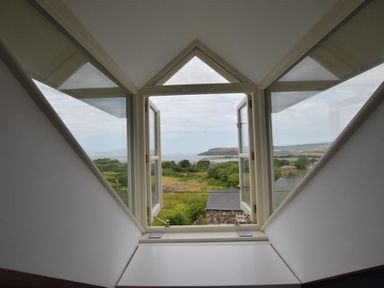 An open window with triangular glass panels on either side overlooking greenery and a distant coastline at Gwelfor Newport in Newport Pembrokeshire