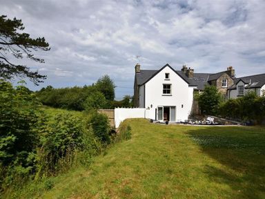A white house with an open door and a garden with grass and patio furniture at Gwelfor Newport in Newport Pembrokeshire