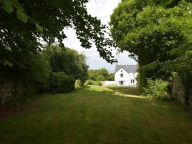 A grassy garden area with trees and bushes surrounding a white house at Gwelfor Newport in Newport Pembrokeshire