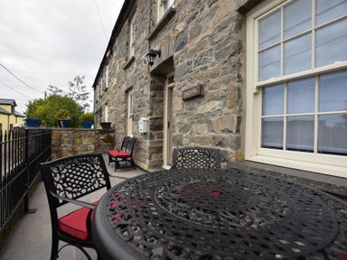 An outdoor patio area with a black metal table and chairs with red cushions next to a stone building at Gwelfor Newport in Newport Pembrokeshire