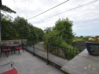 A patio with outdoor table and chairs with red cushions overlooking a road and green trees at Gwelfor Newport in Newport Pembrokeshire