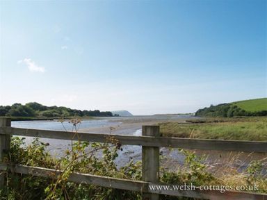A river with grassy banks and a wooden fence in the foreground at Gwelfor Newport in Newport Pembrokeshire