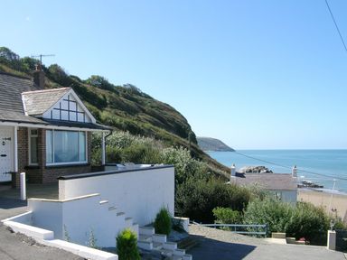 A coastal house with white walls next to a hillside overlooking the sea at Delyn Aur in Tresaith Ceredigion