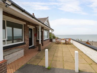 An outdoor patio with a table and chairs overlooking the sea at Delyn Aur, Tresaith, Ceredigion