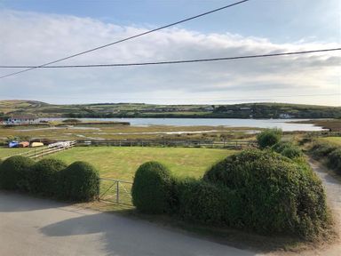 A fenced grassy area with bushes near a body of water and hills at Neverndale in Newport Pembrokeshire