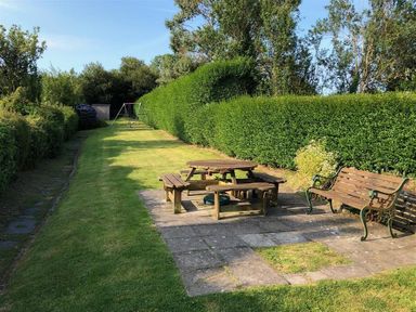 A garden with a wooden picnic table, bench, swings, and surrounding hedges at Neverndale in Newport Pembrokeshire