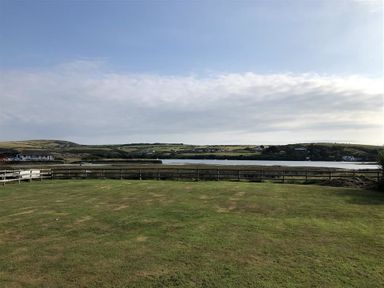 A grassy field fenced with wooden rails overlooking a body of water with hills and houses in the background at Neverndale in Newport Pembrokeshire