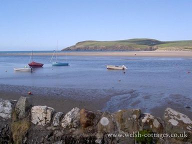 A coastal scene with small boats on water a sandy beach and grassy hills in the background at Neverndale in Newport Pembrokeshire