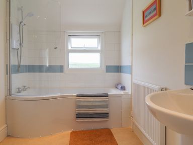 A bathroom with a bathtub shower combination a window above and a sink at Neverndale in Newport Pembrokeshire