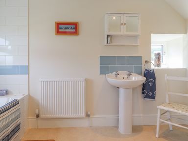 A bathroom with a pedestal sink a towel hanging a chair and a radiator at Neverndale in Newport Pembrokeshire