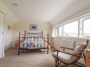 A bedroom with a metal bed frame floral bedding bedside tables lamps a wooden chair and a row of windows at Neverndale in Newport Pembrokeshire