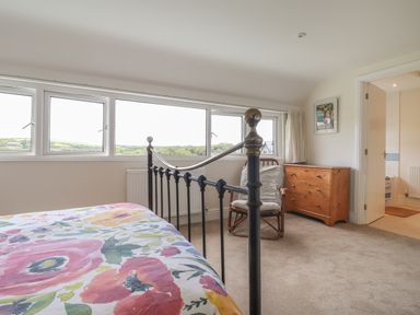 A bedroom with a floral bedspread a black metal bed frame a wooden chest of drawers and a chair at Neverndale in Newport Pembrokeshire
