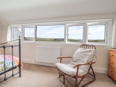A bedroom with a metal bed frame a wooden chair with cushion a wooden dresser and four small windows at Neverndale in Newport Pembrokeshire