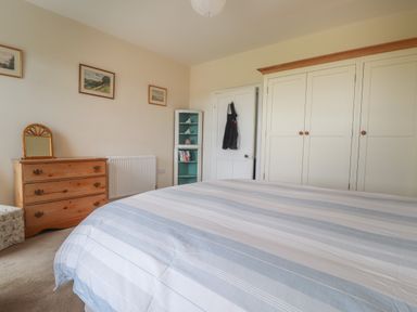 A bedroom with a bed striped bedding a wooden chest of drawers a small corner shelf and built-in wardrobes at Neverndale in Newport Pembrokeshire
