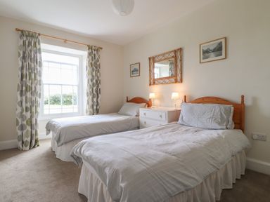 A bedroom with two single beds a window with curtains and a dresser with lamps at Neverndale in Newport Pembrokeshire
