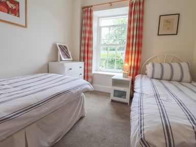 A bedroom with two single beds and a window with red plaid curtains at Neverndale in Newport Pembrokeshire