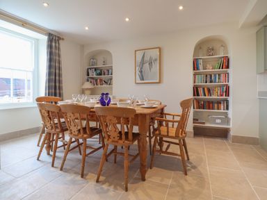 A dining room with wooden table and chairs set with bowls and glasses near bookshelves at Neverndale in Newport Pembrokeshire
