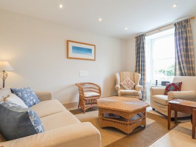 A living room with a sofa armchairs wicker coffee table and window with curtains at Neverndale Newport Pembrokeshire