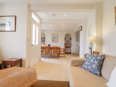 A living room with a beige sofa and a wicker ottoman leading to a dining area with a wooden table and chairs at Neverndale in Newport Pembrokeshire