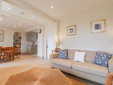 A living room with a beige sofa and blue pillows next to a wooden dining table and a bookshelf at Neverndale in Newport Pembrokeshire