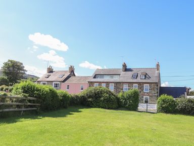 A grassy yard with bushes and a wooden fence in front of a row of stone and pink houses at Neverndale in Newport Pembrokeshire