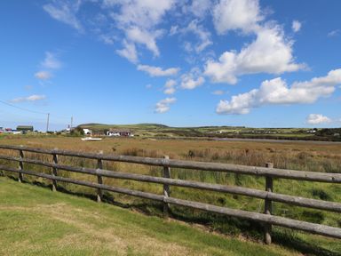 A wooden fence with grass and fields under a blue sky with clouds at Neverndale in Newport Pembrokeshire