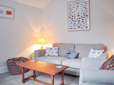 A living room with a beige sofa with pillows a wooden coffee table a lamp and framed pictures on the walls at Neverndale in Newport Pembrokeshire
