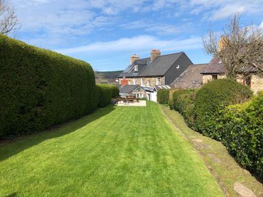 A long grass lawn with hedges on both sides and a picnic table near stone houses at Neverndale in Newport Pembrokeshire