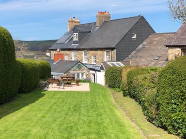 A backyard with trimmed hedges wooden bench and picnic table near cottages at Neverndale Newport Pembrokeshire