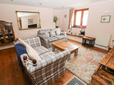 A living room with plaid sofas a wooden coffee table a large mirror and a patterned rug at Mill Barn Denant in Haverfordwest Pembrokeshire