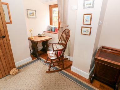 A corner of a room with a wooden rocking chair a small wooden table with a lamp books on a windowsill and framed pictures on the wall at Mill Barn Denant Haverfordwest Pembrokeshire
