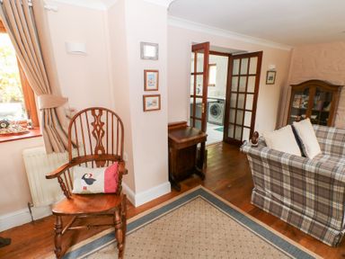 A living room with a wooden chair with a puffin cushion a plaid sofa with white pillows a wooden cabinet and a small wooden table at Mill Barn Denant in Haverfordwest Pembrokeshire