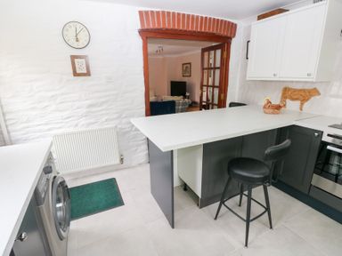 A kitchen with a white countertop bar stool washing machine and doorway leading to a living room at Mill Barn Denant in Haverfordwest Pembrokeshire