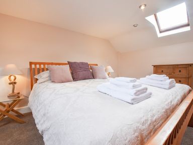 A bedroom with a wooden bed with pillows and folded towels a wooden dresser and bedside tables with lamps at Mill Barn Denant Haverfordwest Pembrokeshire