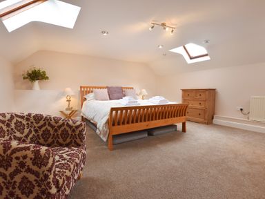A bedroom with a wooden bed and patterned armchair under skylights at Mill Barn Denant in Haverfordwest Pembrokeshire