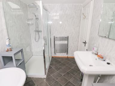 A bathroom with a glass shower enclosure a white sink a gray storage unit a towel rack and tiled floor at Mill Barn Denant in Haverfordwest Pembrokeshire