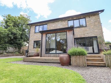 The back of a two-story stone house with large windows wooden deck steps and garden with grass and plants at Ty Cerrig in Newport Pembrokeshire