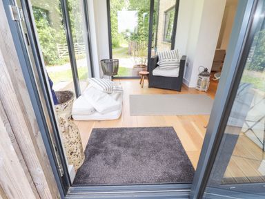 A seating area with a wicker chair cushions rugs and large windows showing a garden at Ty Cerrig Newport Pembrokeshire