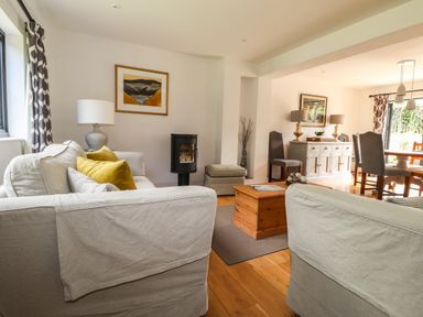 A living room with sofas coffee table and lamp opening into a dining area with chairs and sideboard at Ty Cerrig Newport Pembrokeshire