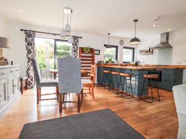 A kitchen and dining area with a wooden dining table and chairs a kitchen island with bar stools and pendant lights at Ty Cerrig in Newport Pembrokeshire