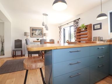 A kitchen island with wooden countertop and blue drawers with stools and a dining area with chairs and a sideboard at Ty Cerrig Newport Pembrokeshire