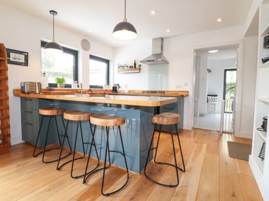 A kitchen with a wooden floor a blue island with four wooden stools two windows and a silver stove at Ty Cerrig in Newport Pembrokeshire