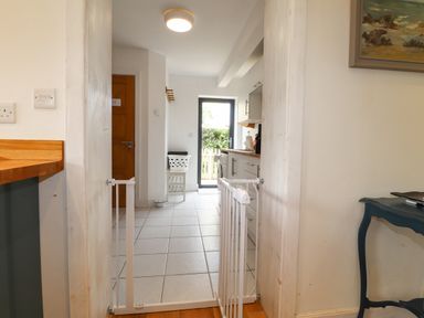 A kitchen with tiled floor white baby gate and wooden door with chair and laundry basket at Ty Cerrig in Newport Pembrokeshire