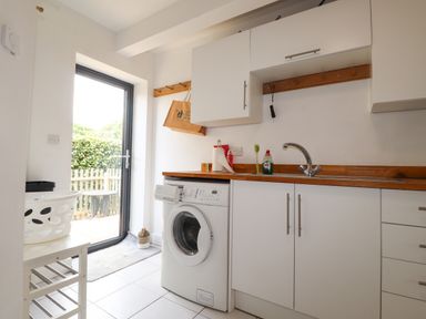 A utility room with a washing machine sink and cabinets and a door leading outside at Ty Cerrig in Newport Pembrokeshire