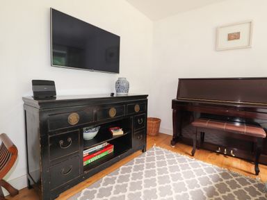 A room with a wall-mounted television a black cabinet with drawers and board games and a piano with a bench at Ty Cerrig in Newport Pembrokeshire